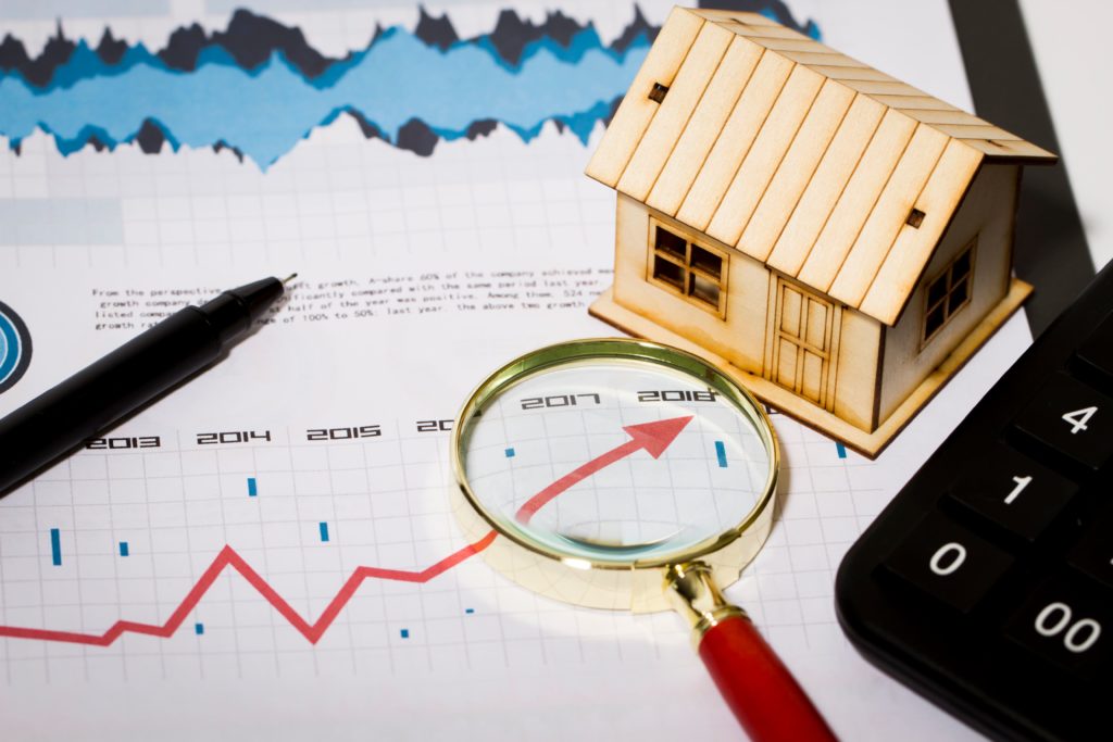 Immobilienbewertung symbolisch dargestellt durch Lupe, die auf einen steigenden Graphen neben einem Hausmodell zeigt