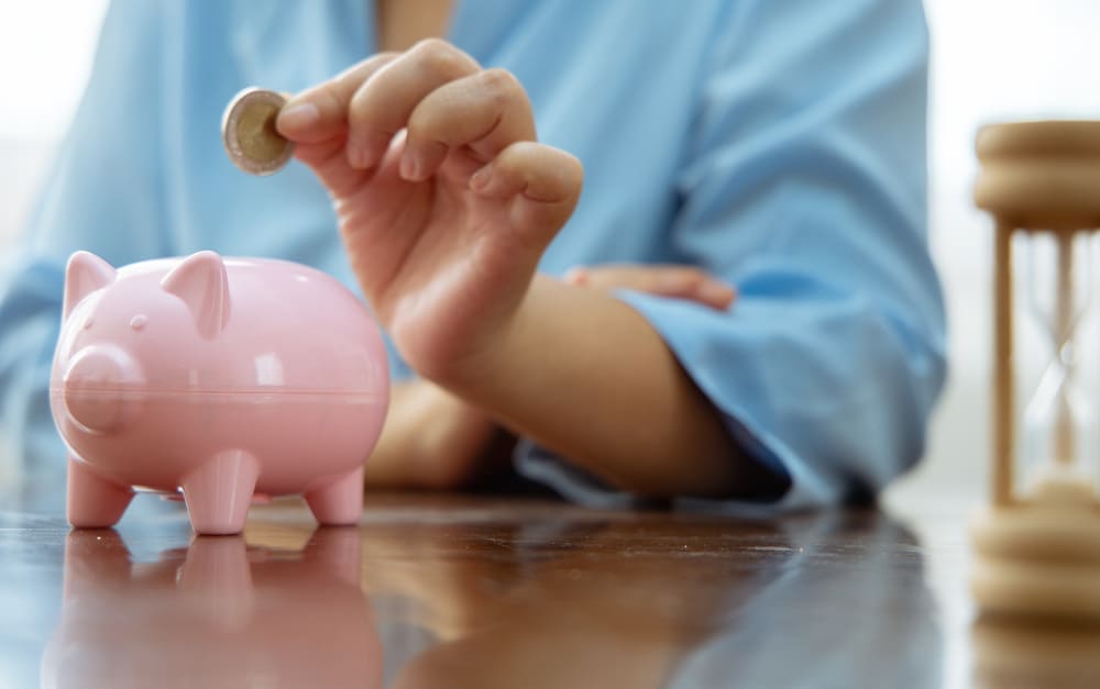 Eine Hand legt eine Münze in ein Sparschwein als Investition.