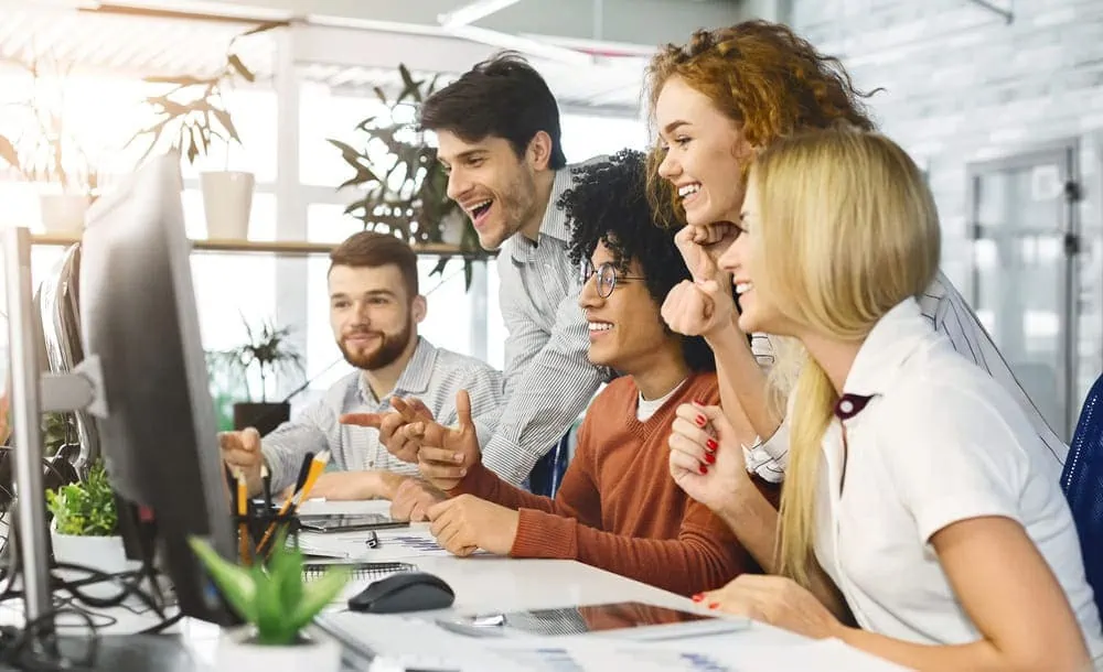 Glückliches und lächelndes Team von Mitarbeitern, das gemeinsam auf einen Computerbildschirm im Büro schaut